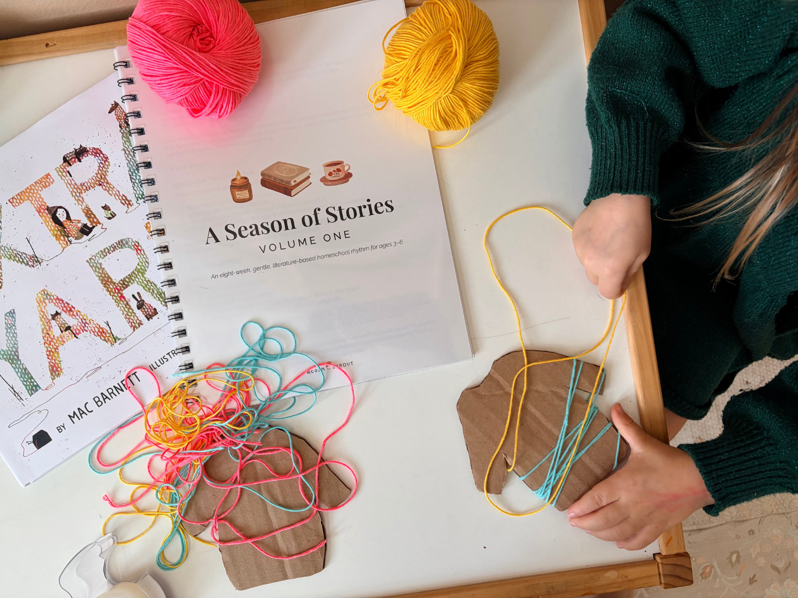 Child working on yarn lacing and sewing activity beside A Season of Stories Volume One homeschool curriculum guide, supporting fine motor development and hands-on learning