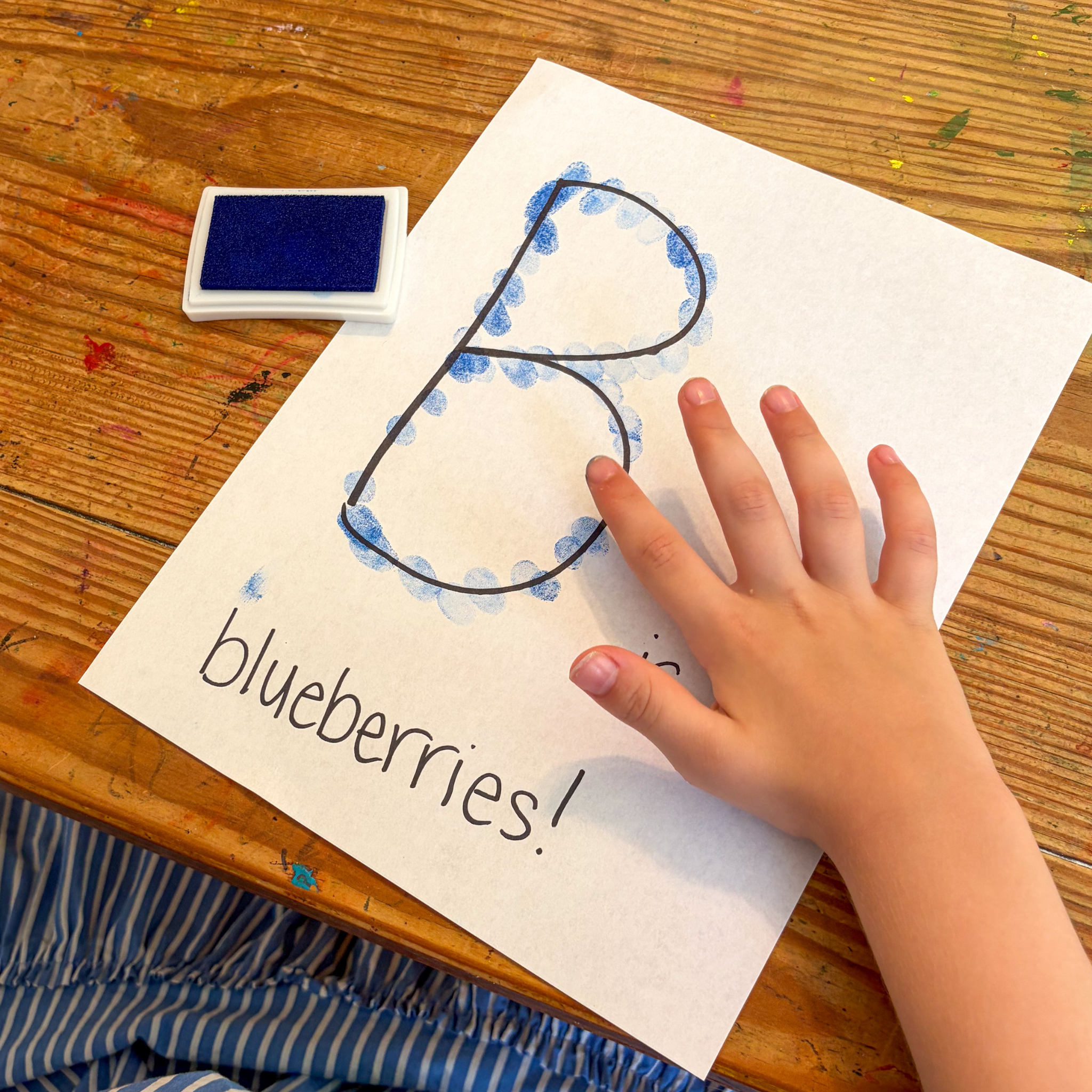 Child making the letter B with blue paint during a Blueberries for Sal preschool literacy activity.