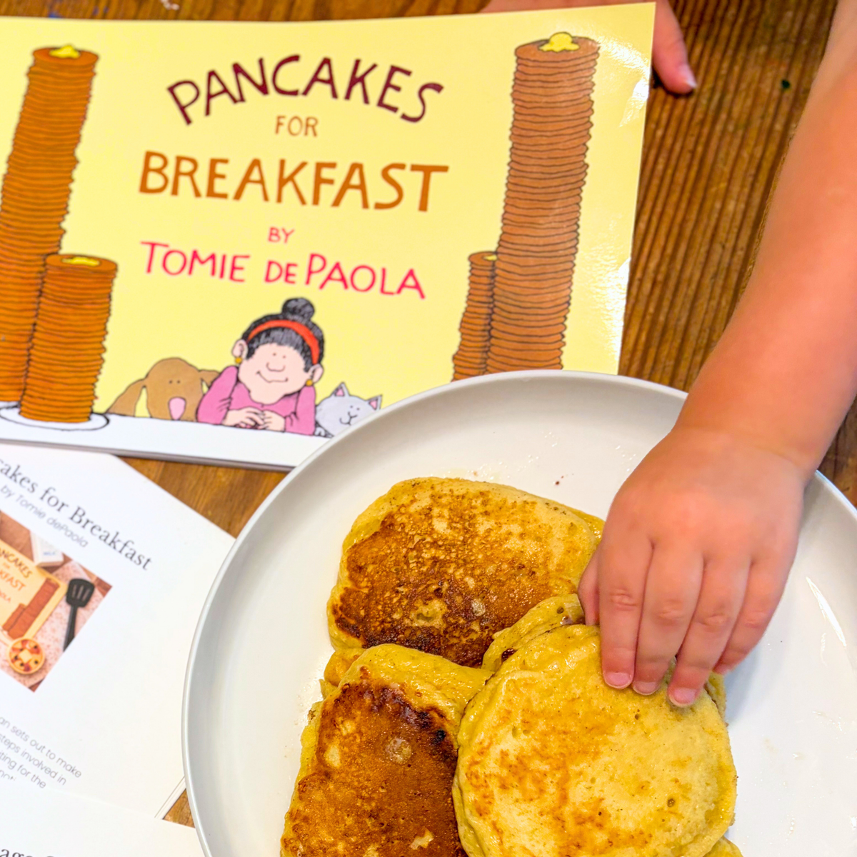 Child reaching for homemade pancakes beside Pancakes for Breakfast and the Acorn to Sprout learning guide.