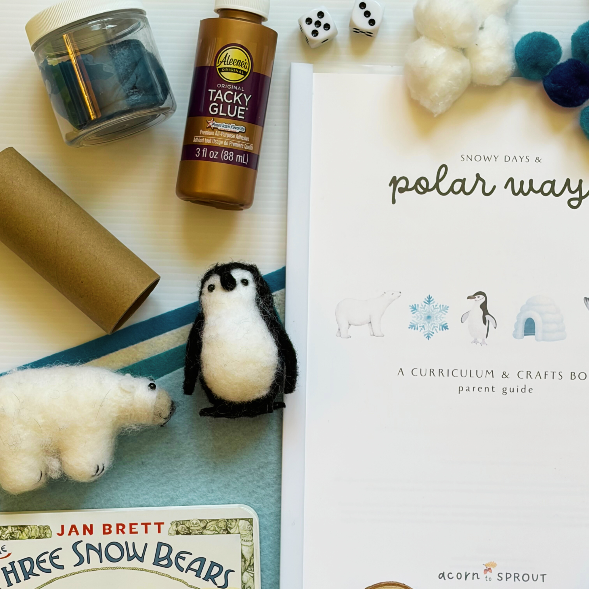 Craft materials and educational items including tacky glue, paper, and a penguin toy on a surface for Acorn to Sprout preschool box.