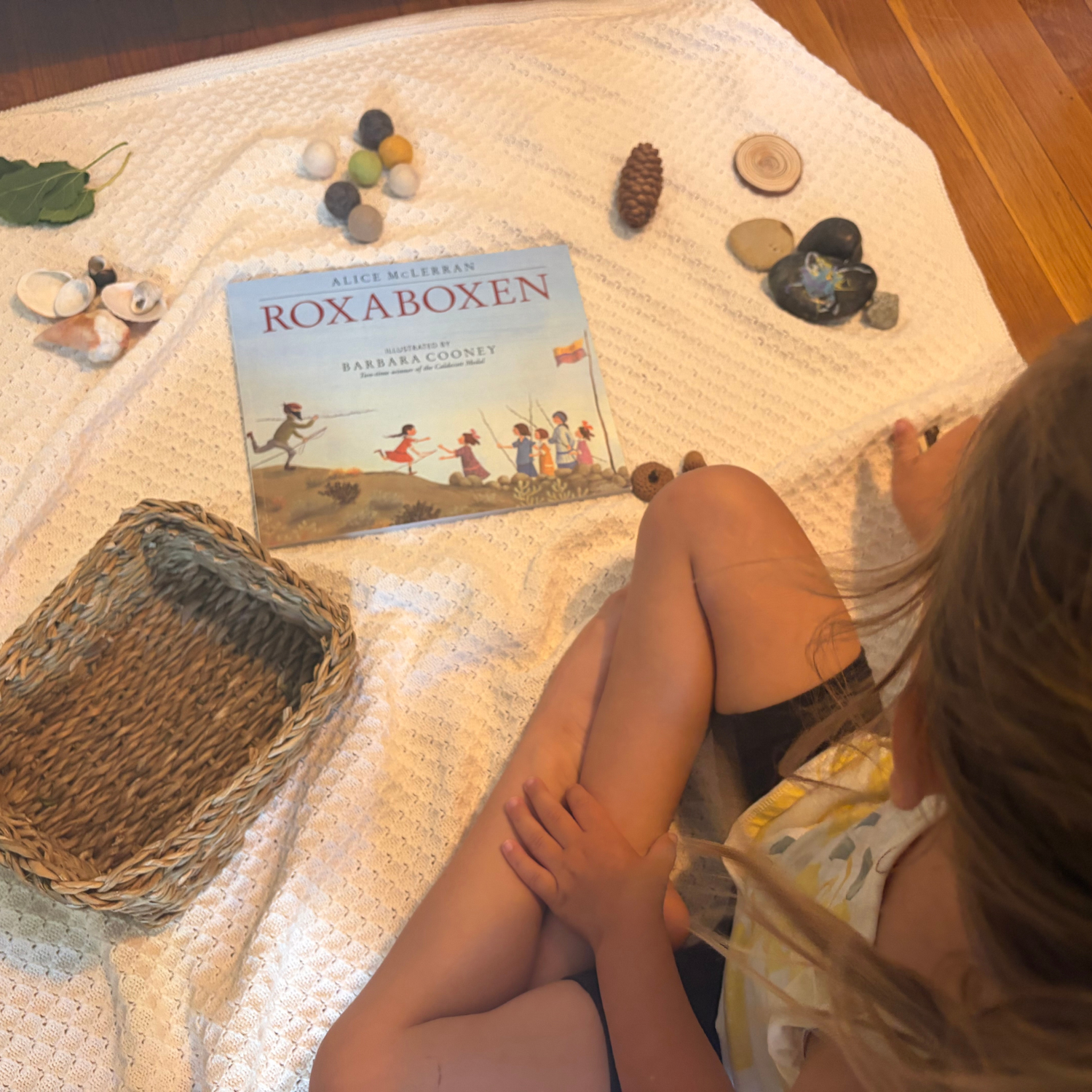Child exploring natural loose parts and imaginative world-building inspired by Roxaboxen as part of a story-based preschool curriculum.