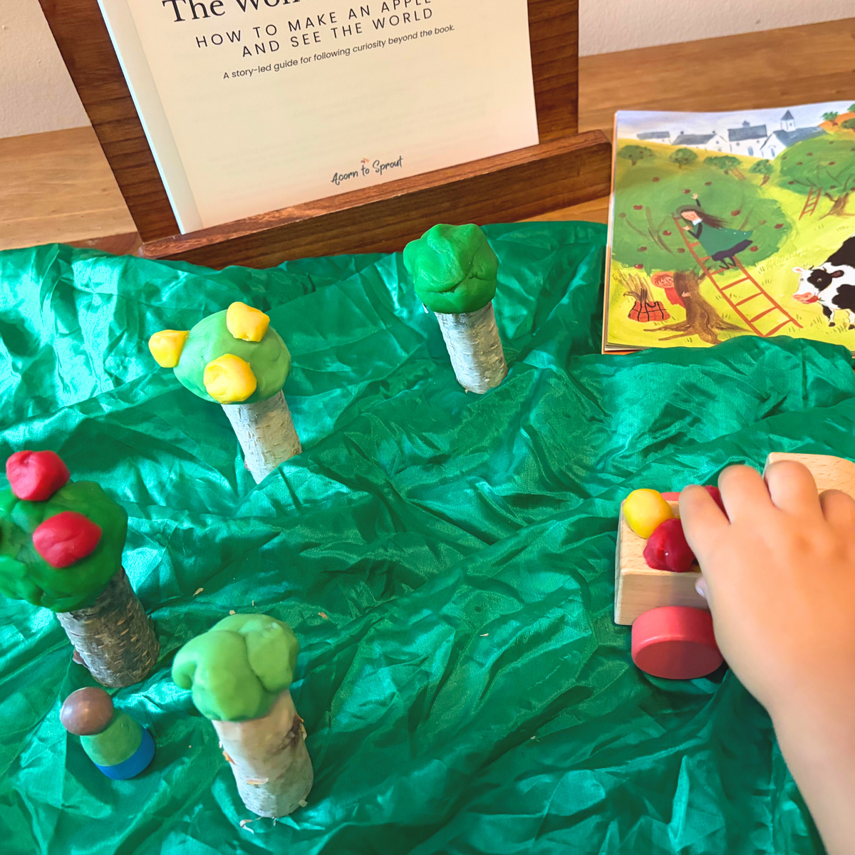 Child playing with a playdough apple orchard inspired by How to Make an Apple Pie and See the World beside The Wonder Continues guide