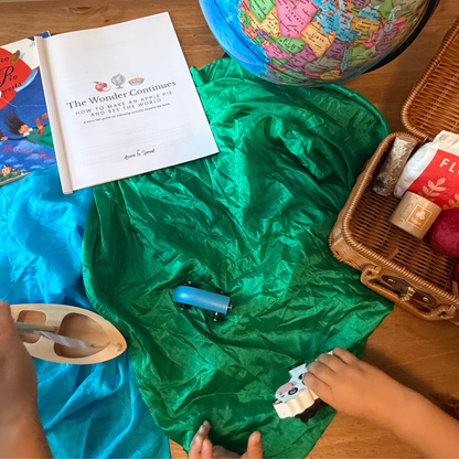 Around-the-world pretend play with a globe, play silks, suitcase, toy vehicles, and The Wonder Continues Apple Pie preschool guide