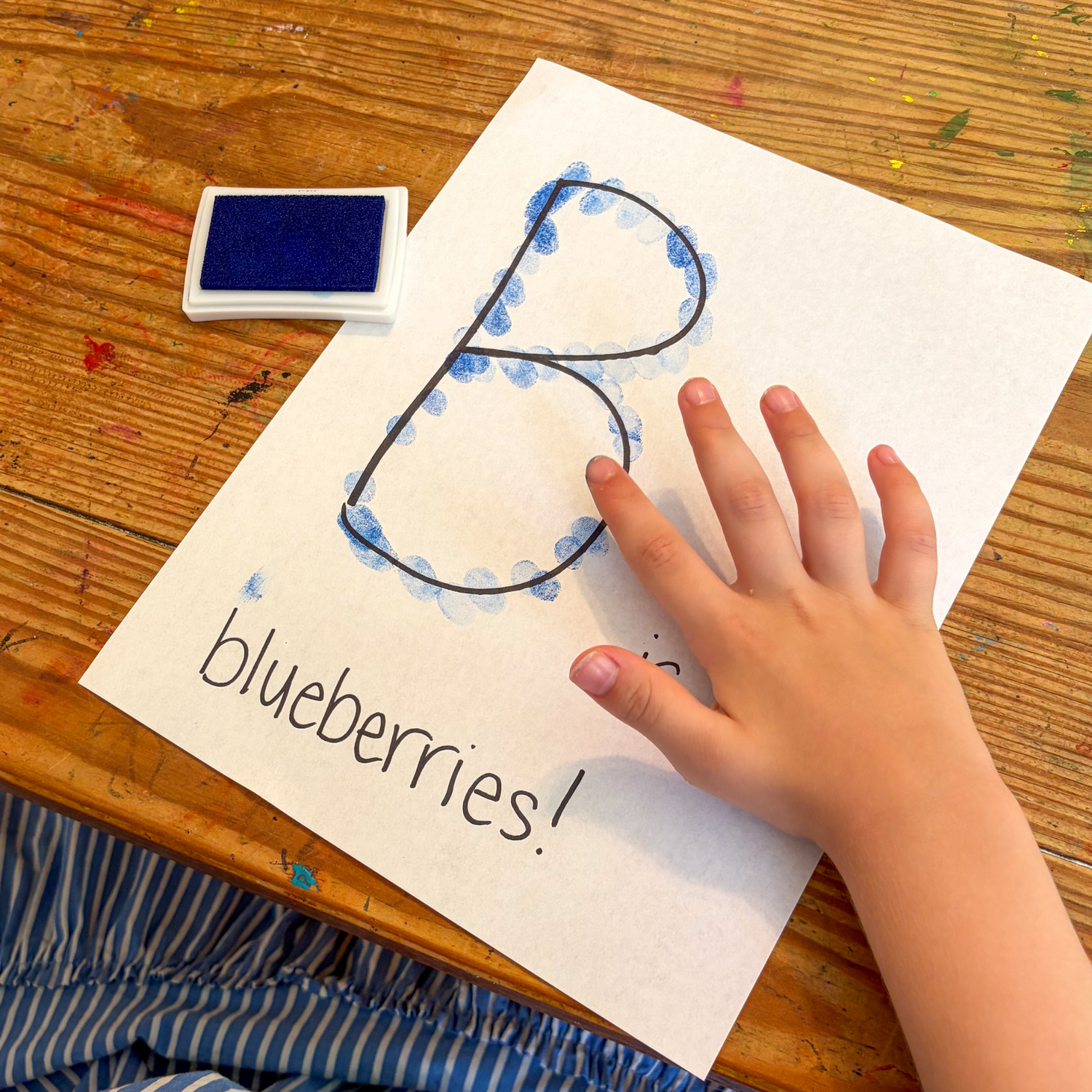 Child making the letter B with blue paint during a Blueberries for Sal preschool literacy activity.