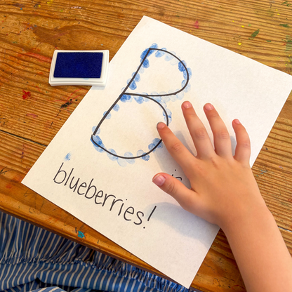 Child making the letter B with blue paint during a Blueberries for Sal preschool literacy activity.