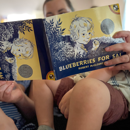 Parent reading Blueberries for Sal by Robert McCloskey with two young children.