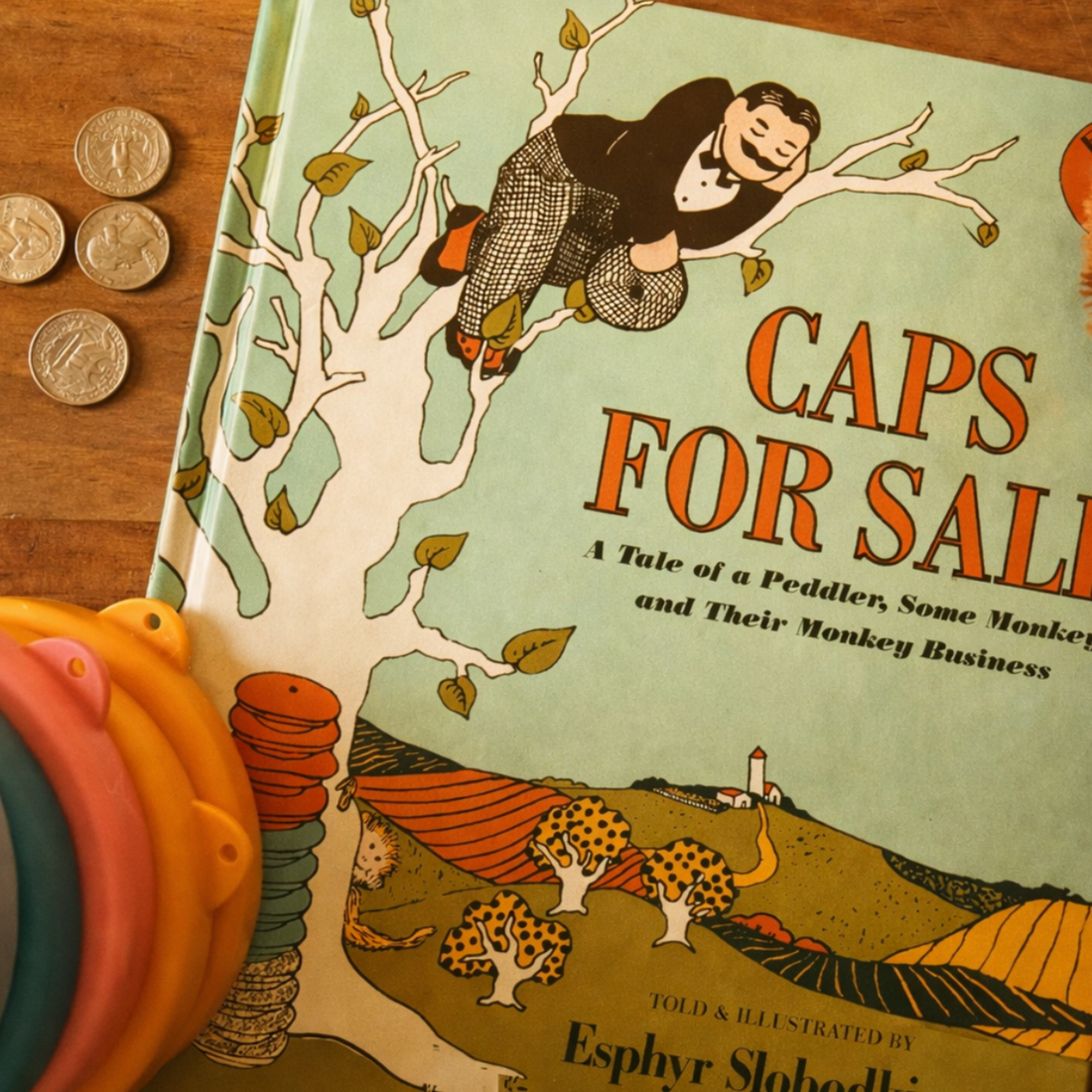 Caps for Sale by Esphyr Slobodkina paired with coins and loose parts, supporting a playful literature-based preschool learning invitation.