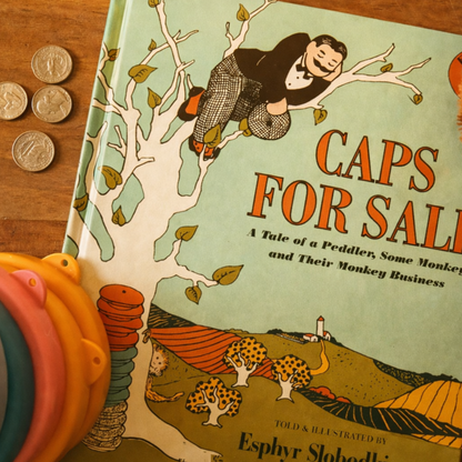 Caps for Sale by Esphyr Slobodkina paired with coins and loose parts, supporting a playful literature-based preschool learning invitation.