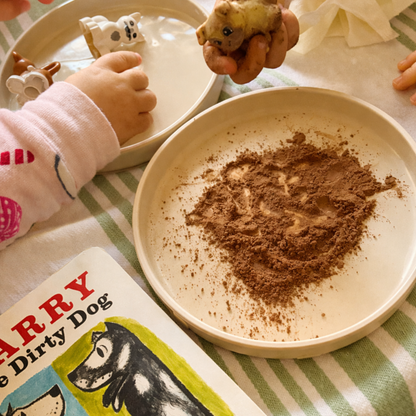 Child making marks in cocoa powder during a sensory activity inspired by Harry the Dirty Dog.