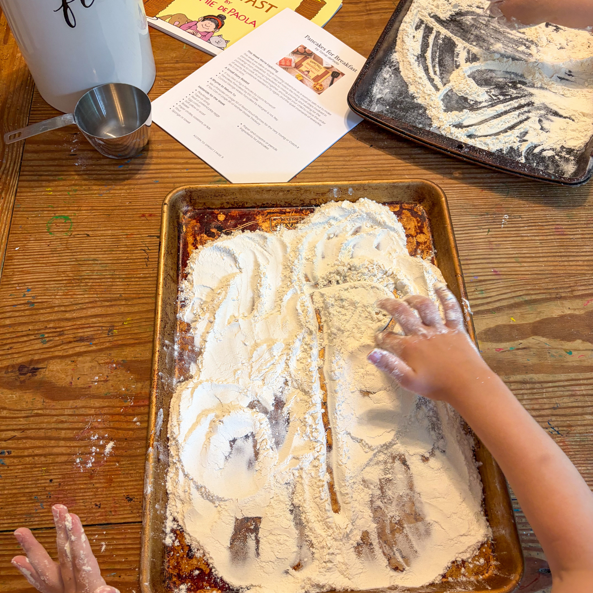 Child drawing in flour during a hands-on activity inspired by Pancakes for Breakfast.