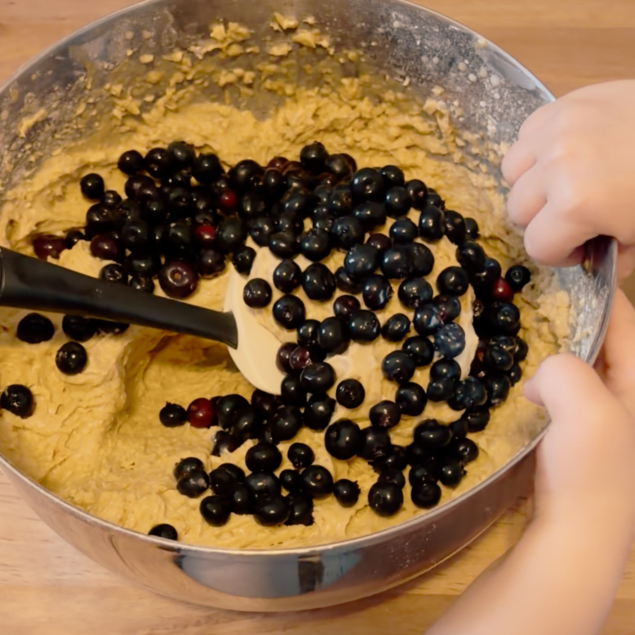 Child adding blueberries to batter during a hands-on baking activity connected to a literature-based homeschool lesson for young children.