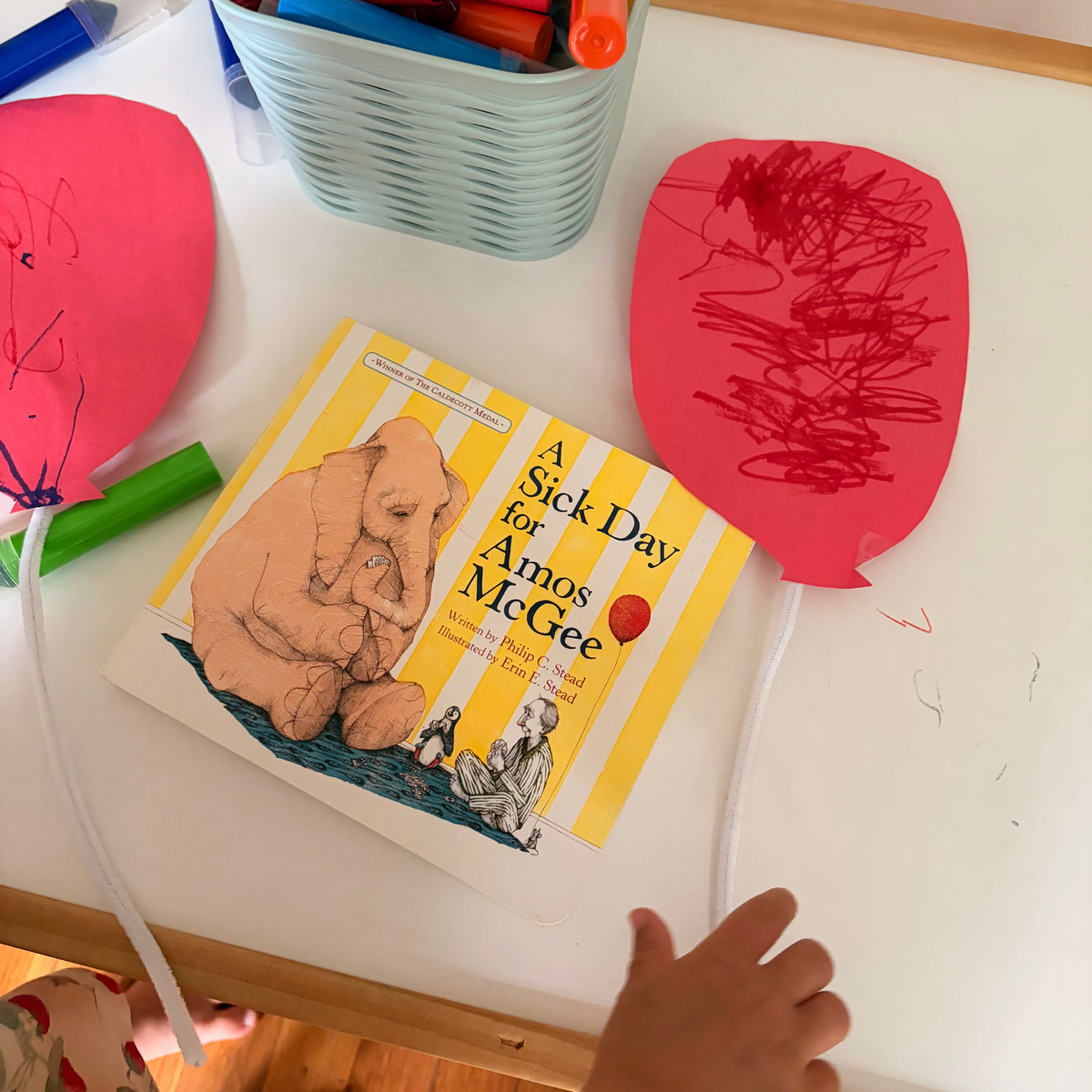 Child drawing and coloring beside A Sick Day for Amos McGee during a simple preschool art activity.