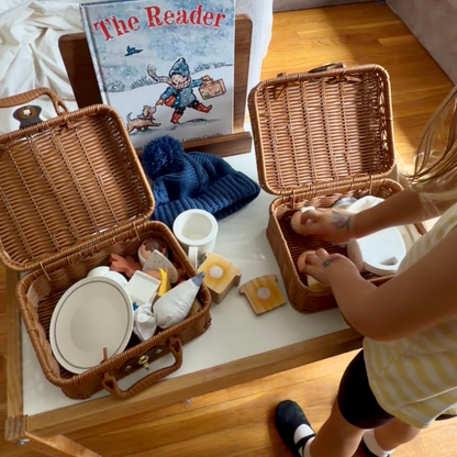 Child exploring winter pretend-play baskets beside The Reader picture book.