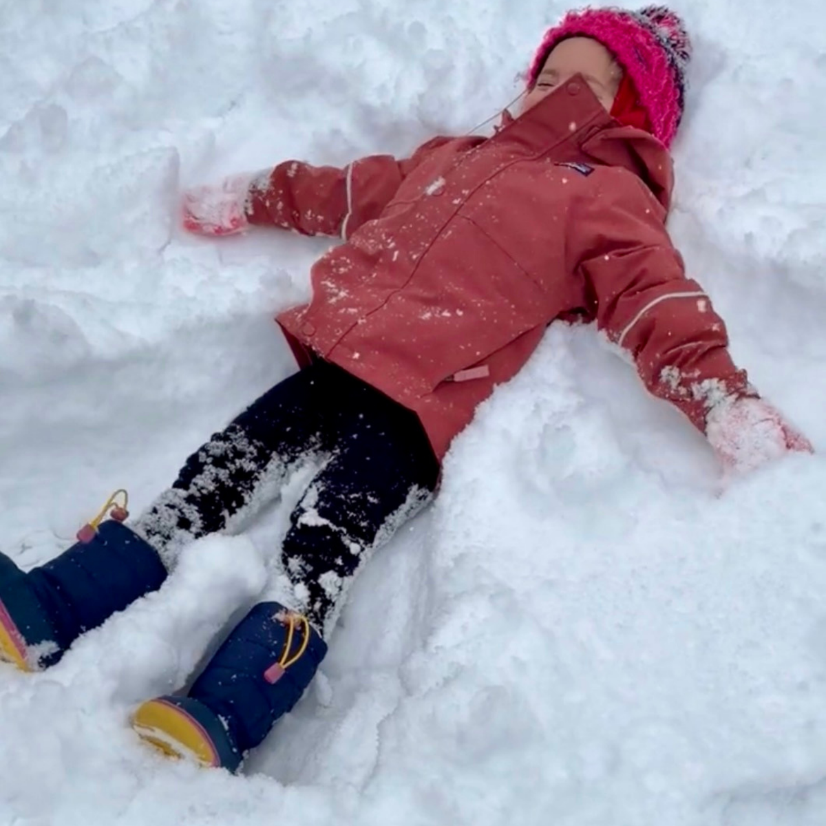 Young child making a snow angel outdoors during a story extension inspired by The Reader.